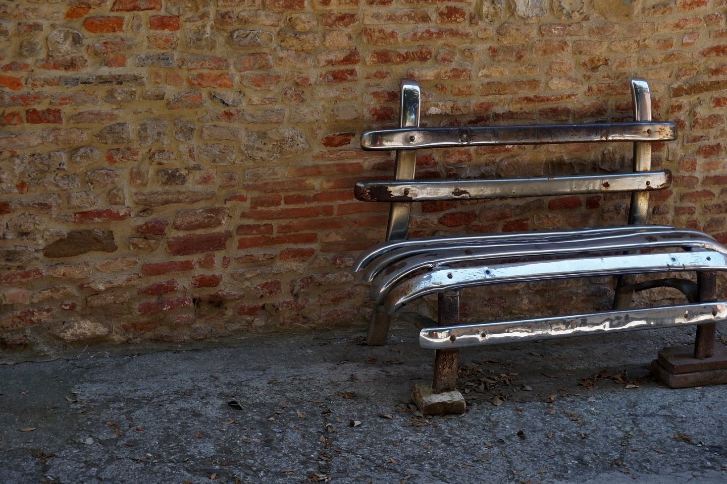 A shiny empty bench made from reused rear car bumpers sits against a brick wall.