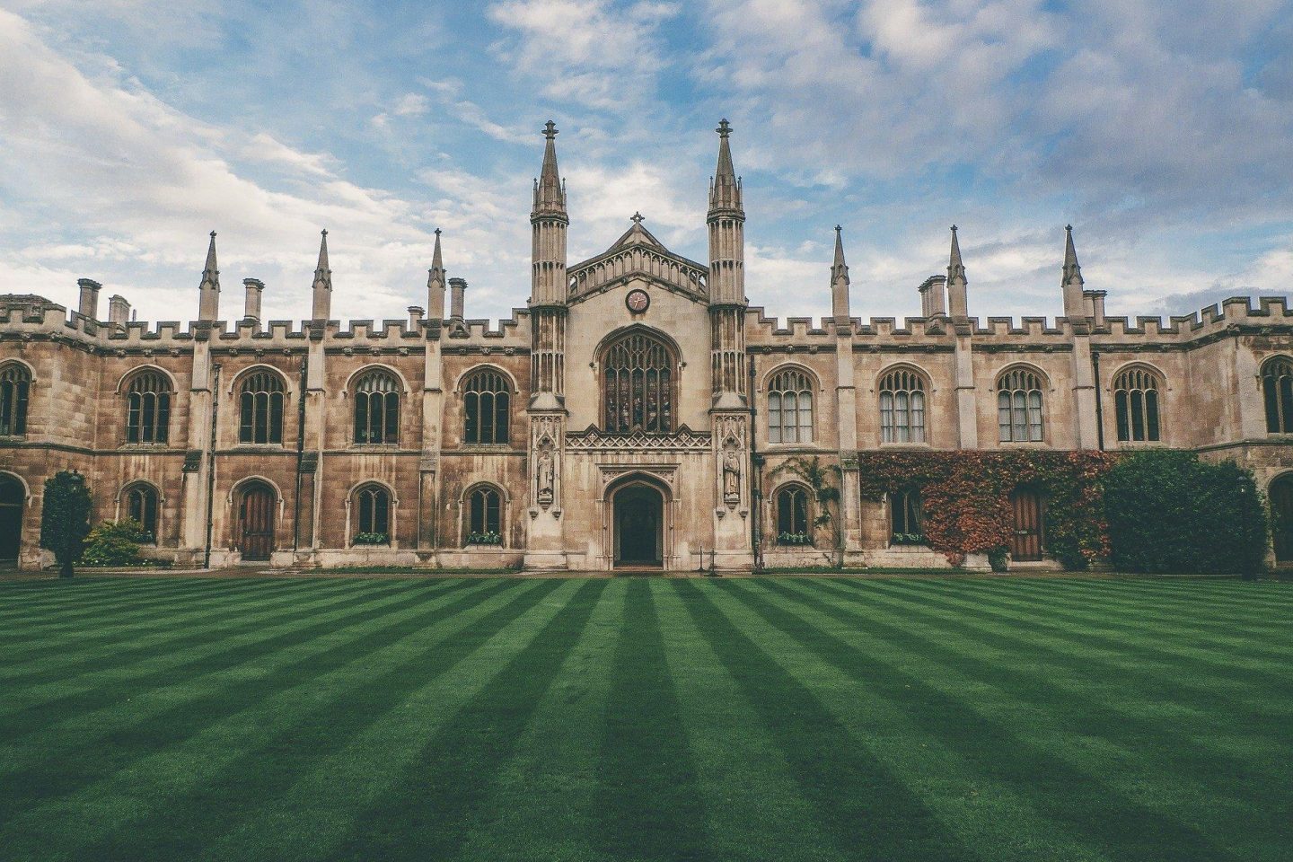 A view of a gothic castle from the front. Before the castle is recently mowed grass.