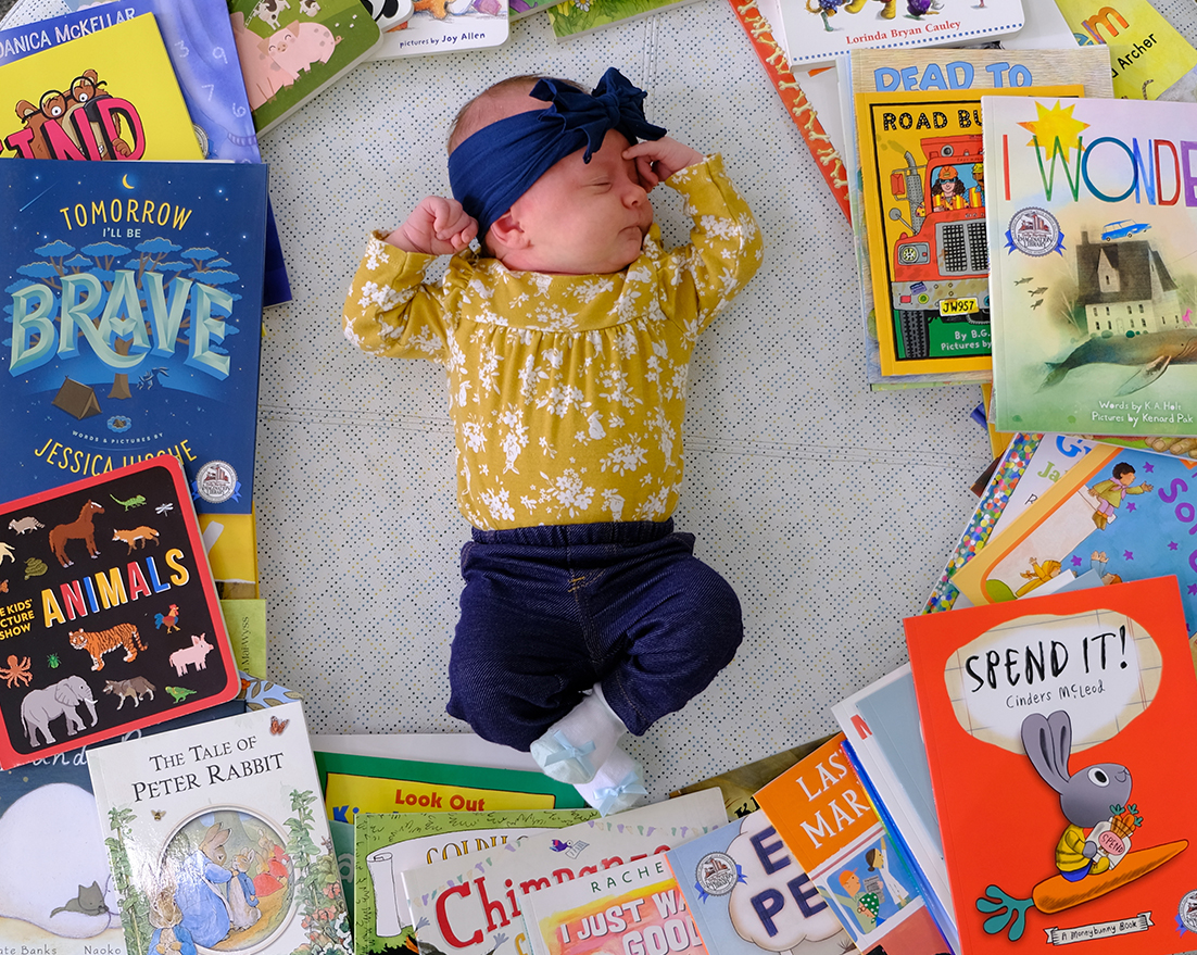imagination library books crop A baby is posed on the floor surrounded by a circle of books from Dolly Parton's Imagination Library.