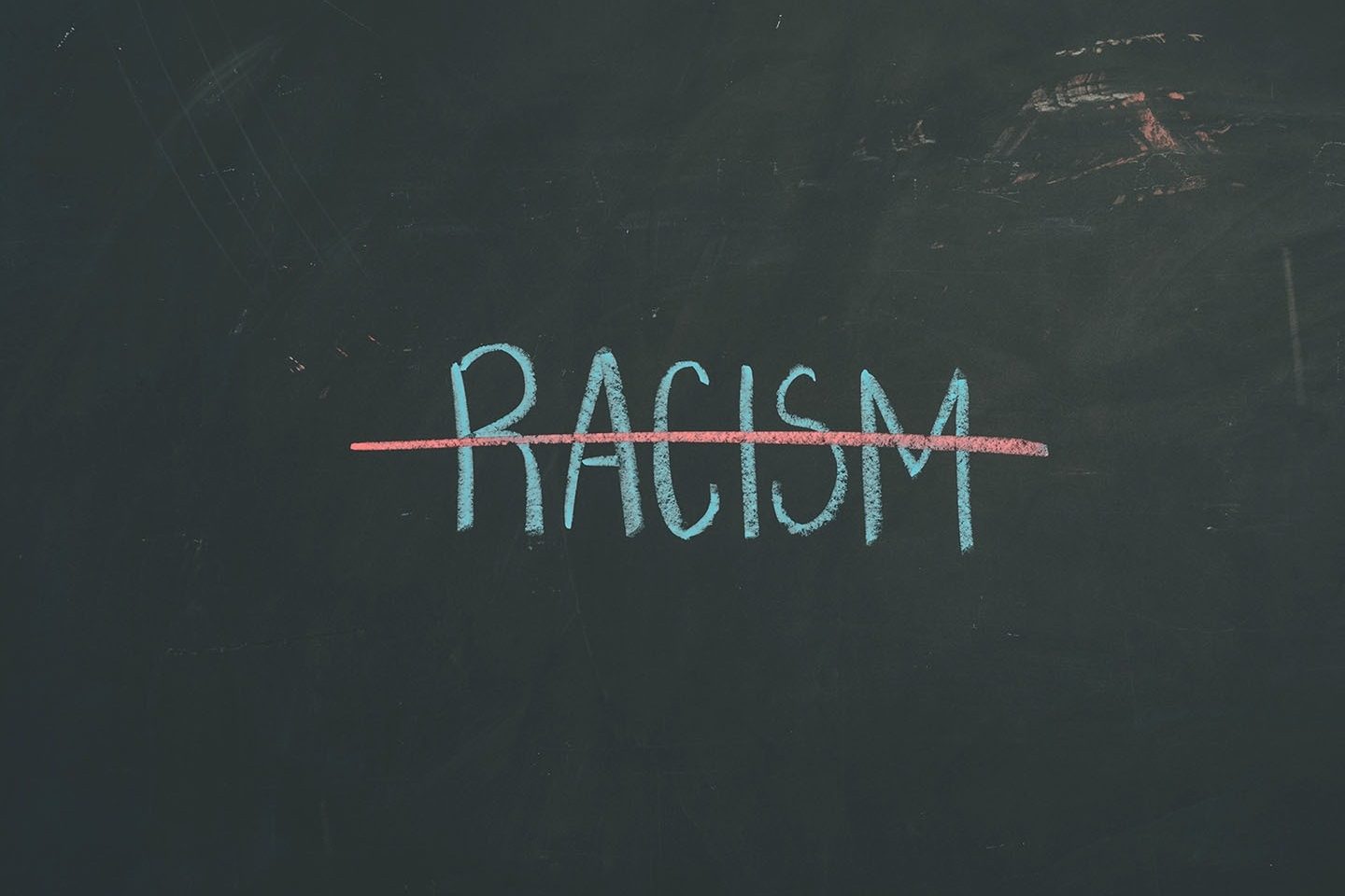 The word racism is written with blue chalk and has a red chalk line drawn through it.
