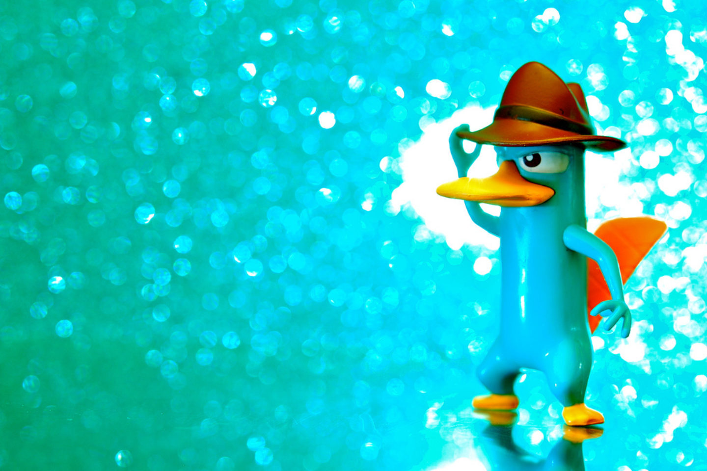 A toy figurine of Perry the Platypus from Disney's "Phineas and Ferb" stands in a sparkly environment that is the same color as his fur.