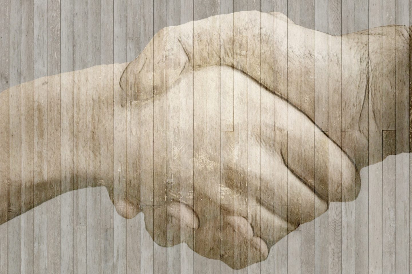 Two hands are clasped in a handshake and are semi-transparent on top of a wall of wooden boards.