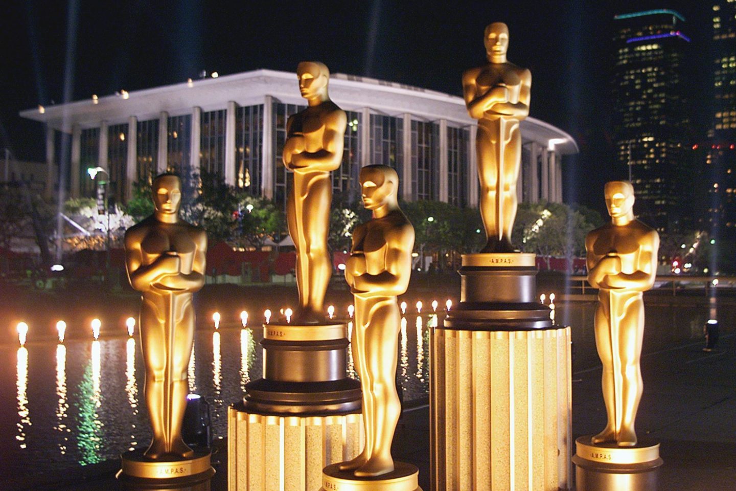 A view of large, life-sized Oscars statues in front of the Los Angeles Music Center at night.