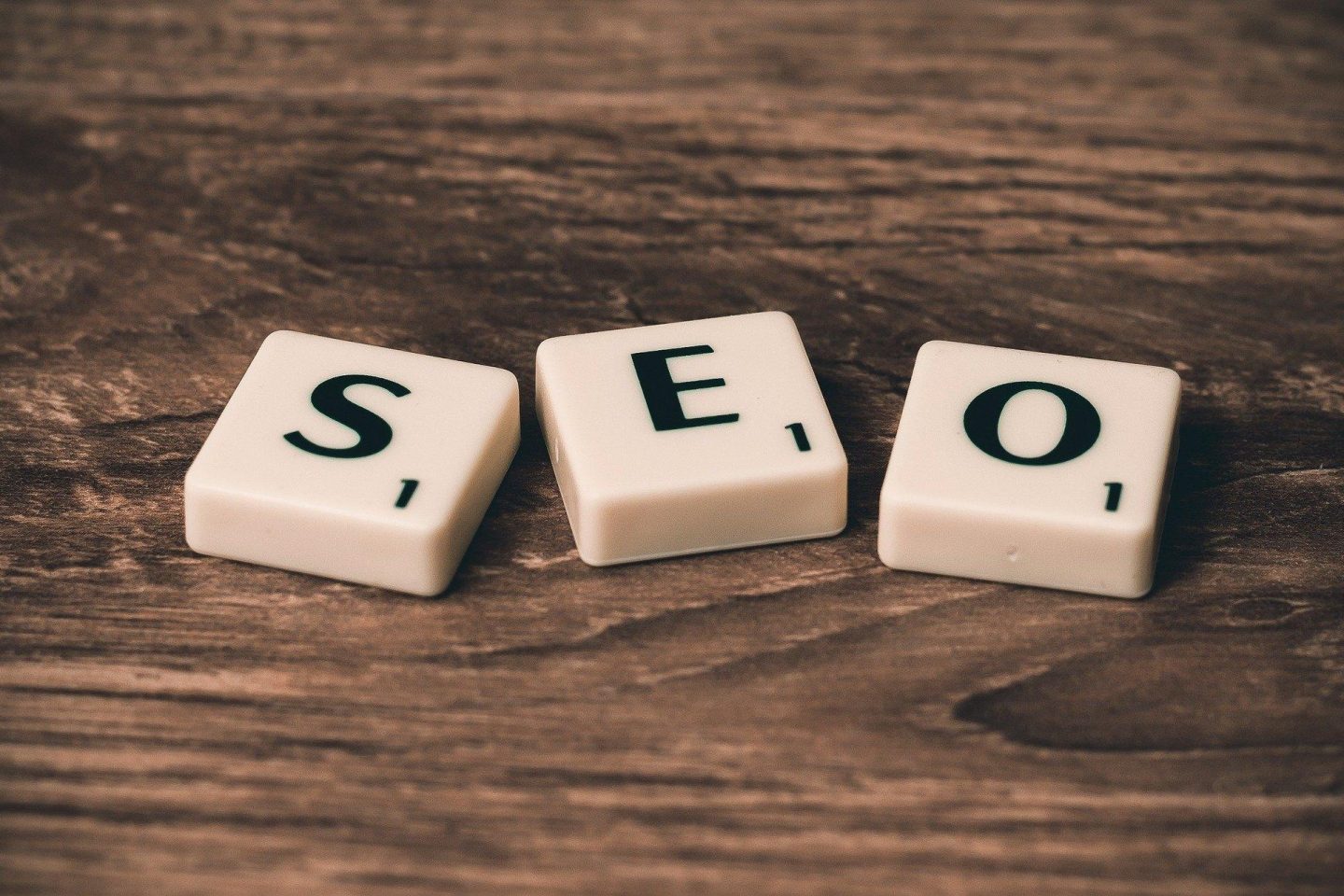 Three scrabble pieces spell out the letters "S," "E," and "O" to create the word "SEO" for "search engine optimization."