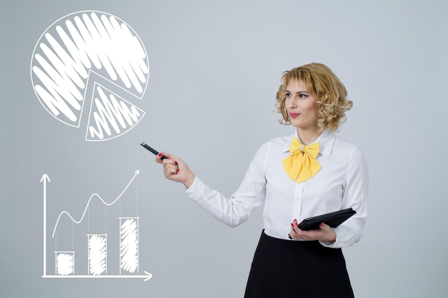 A business woman holds a tablet and stylus while pointing to the open space to her right. In that space are two drawn graphs. The first is a pie chart with a triangle section coming out of the pie graph. The second is a bar graph with an arrow undulating upwards to show growth overtime.