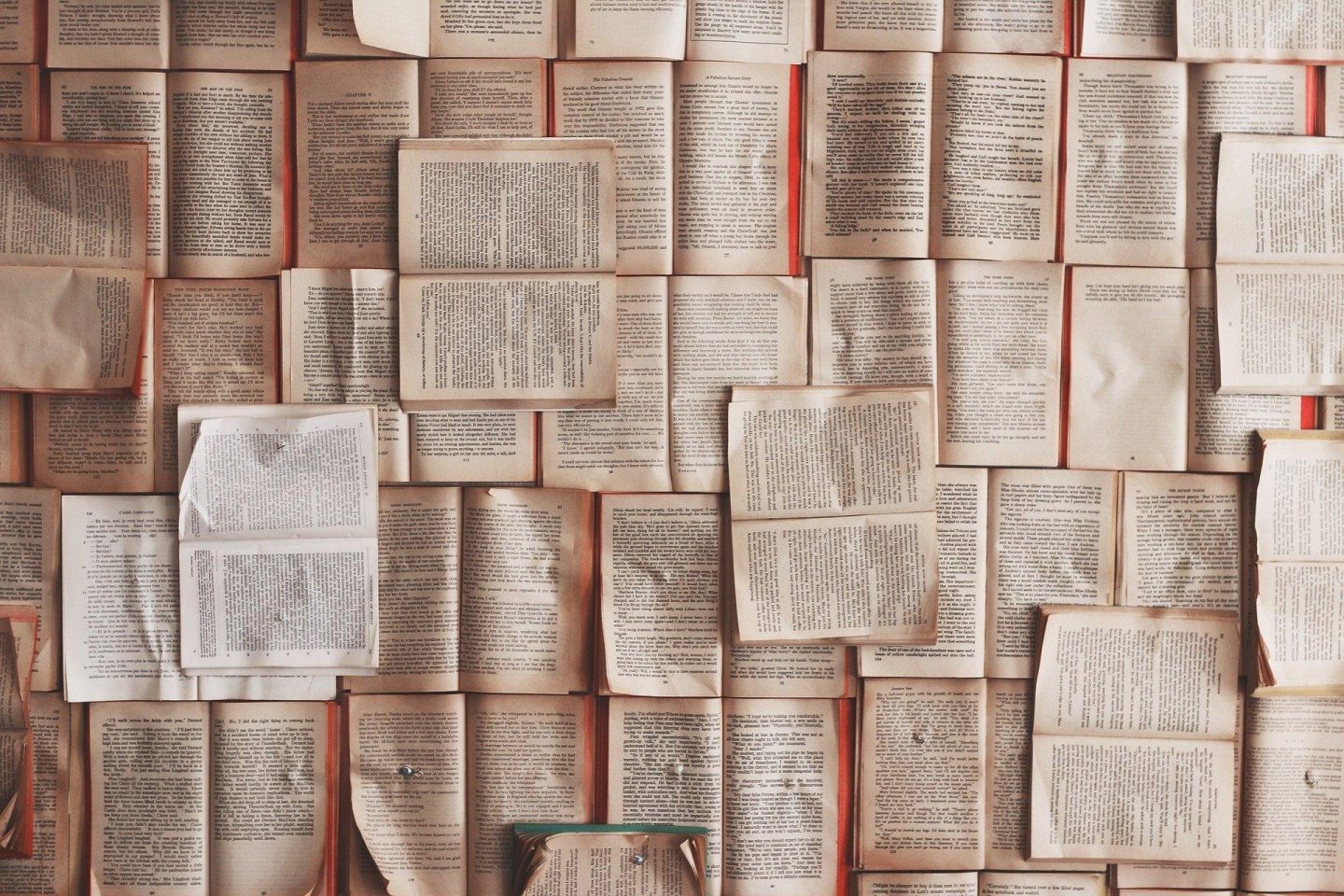 Open books pages are placed next to one another with a few books on top as well to create a grid pattern of books.