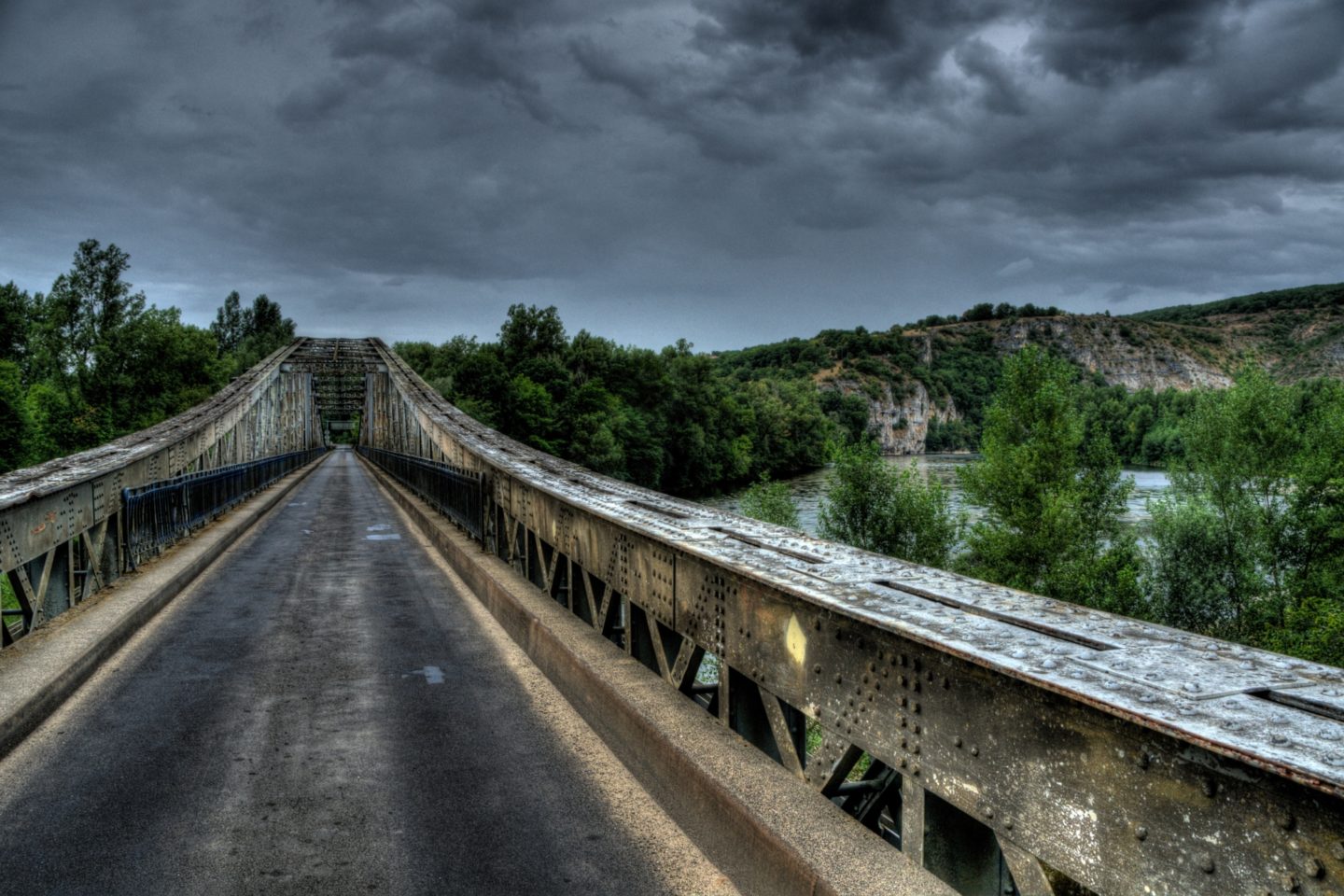 View of an abandoned bridge near a body of water, trees, and hillside.