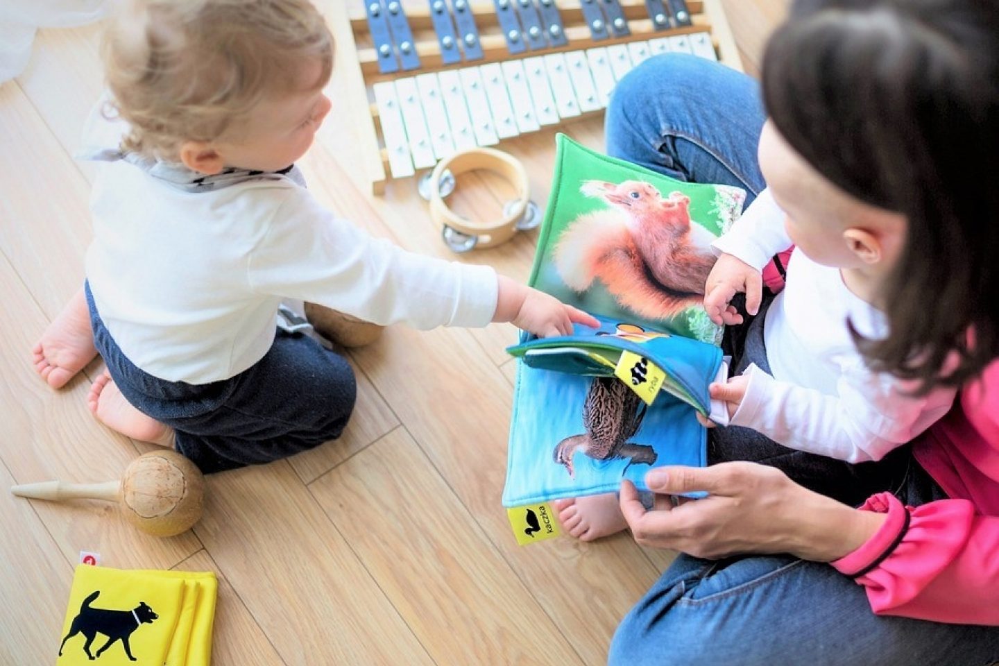 A mother flips through a fabric book with animal images inside with her infant and small toddler.
