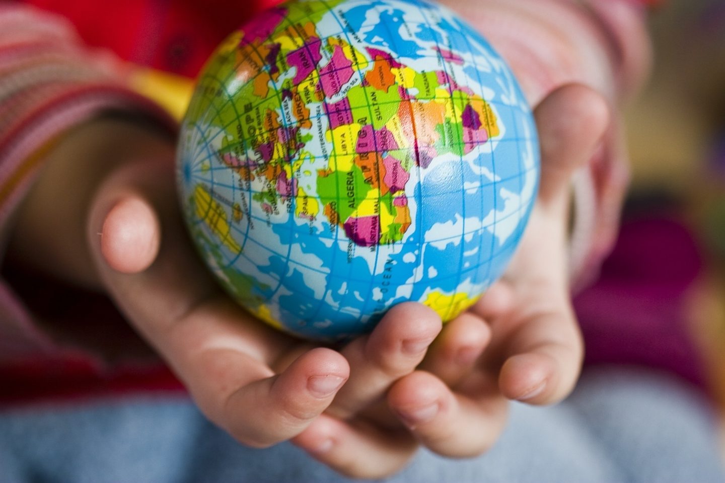 A close up view of a child's hands holding a small colorful globe. The globe is showing the side where Africa is located.
