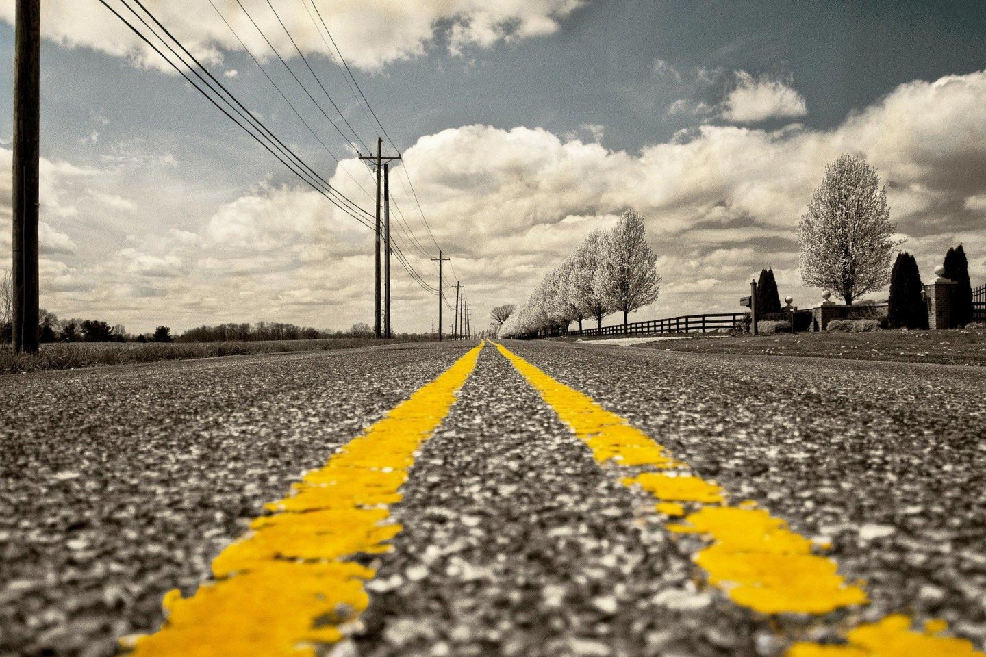 A black and white view of a road with two yellow lines down the center of the road.