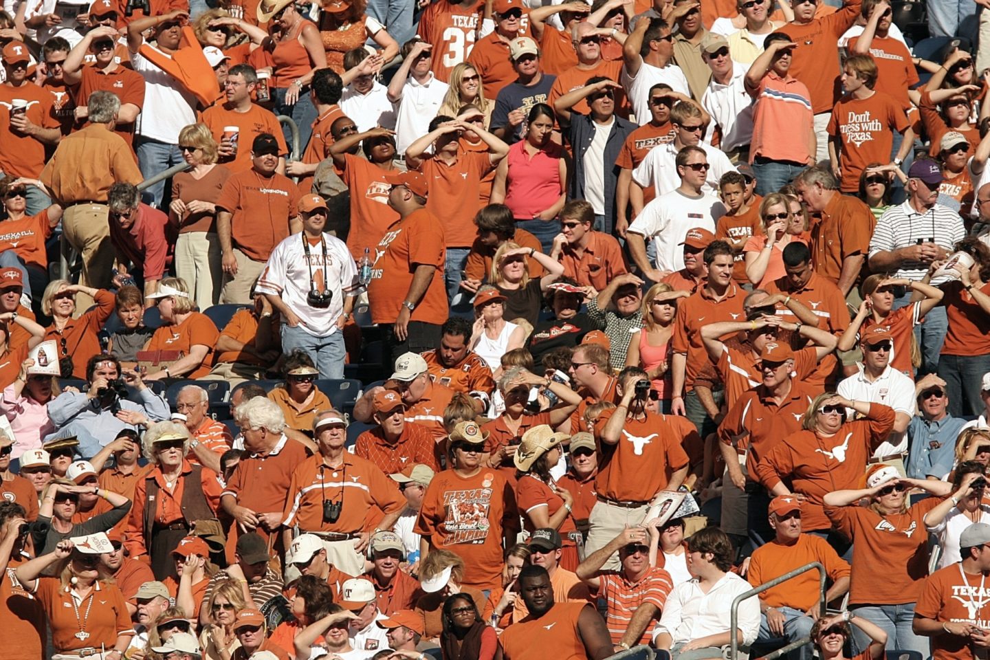 A view of Texas Ranger fans standing in a sunny stadium looking out to the scene before them outside of the image's view.
