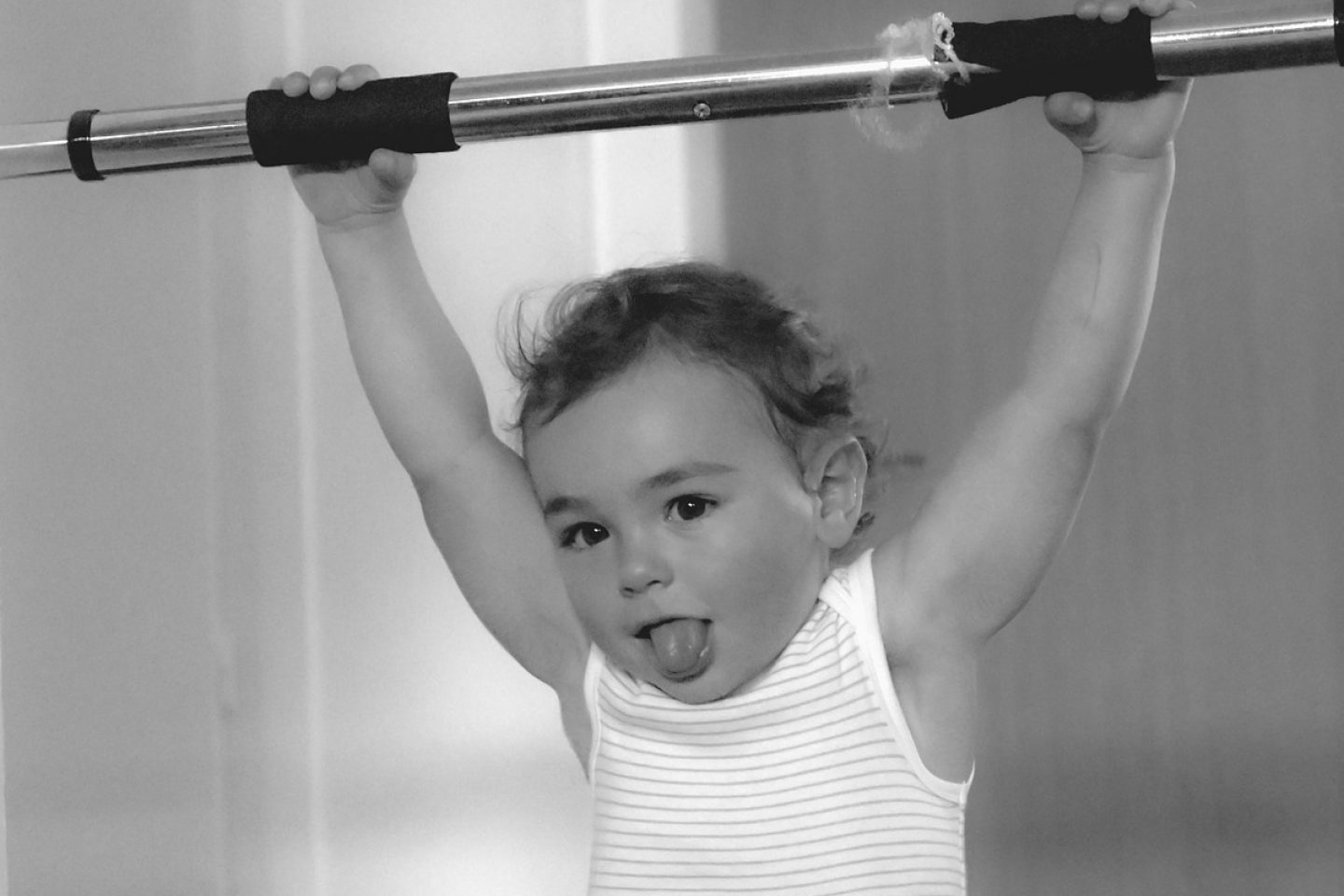 A young toddler holds up a fitness bar with his tongue sticking out.