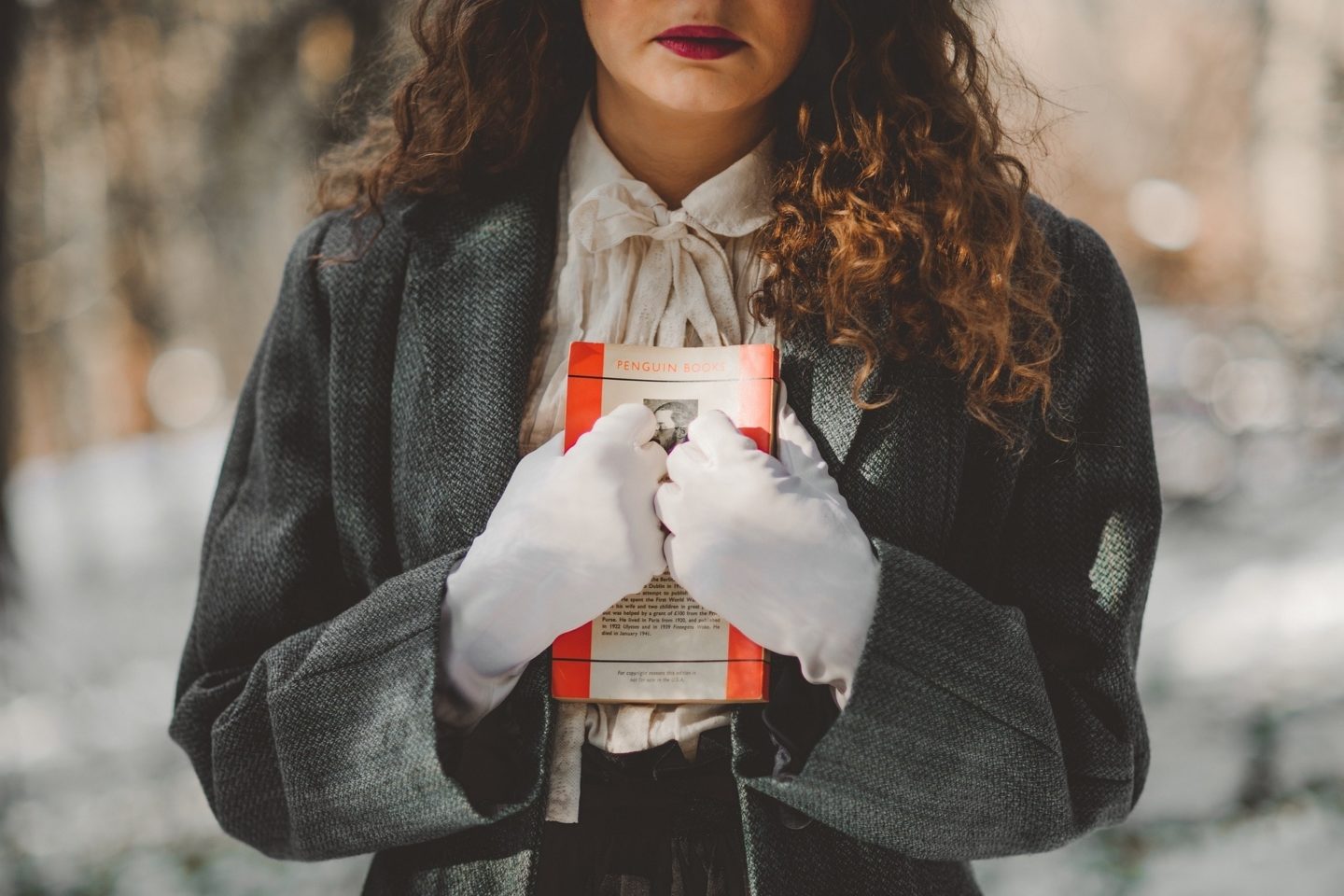 A woman with white gloves on stands outside holding a book against her chest. The book says "Penguin Books" at the top of its back cover.