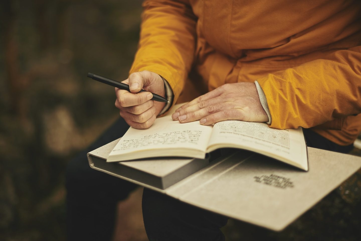 A person's hands are seen holding a notebook open as they write on its lined pages.