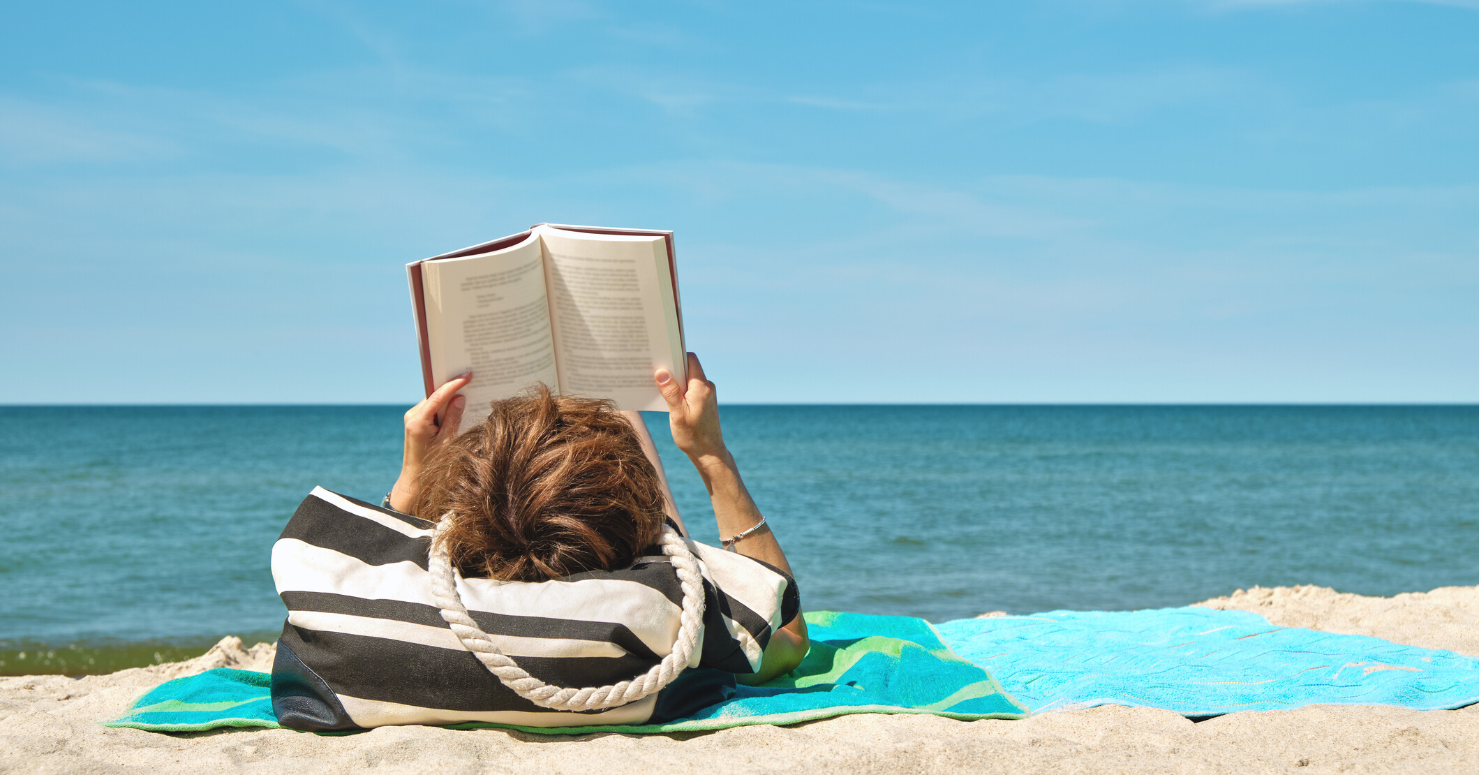 Woman sunbathing on the beach with a book.