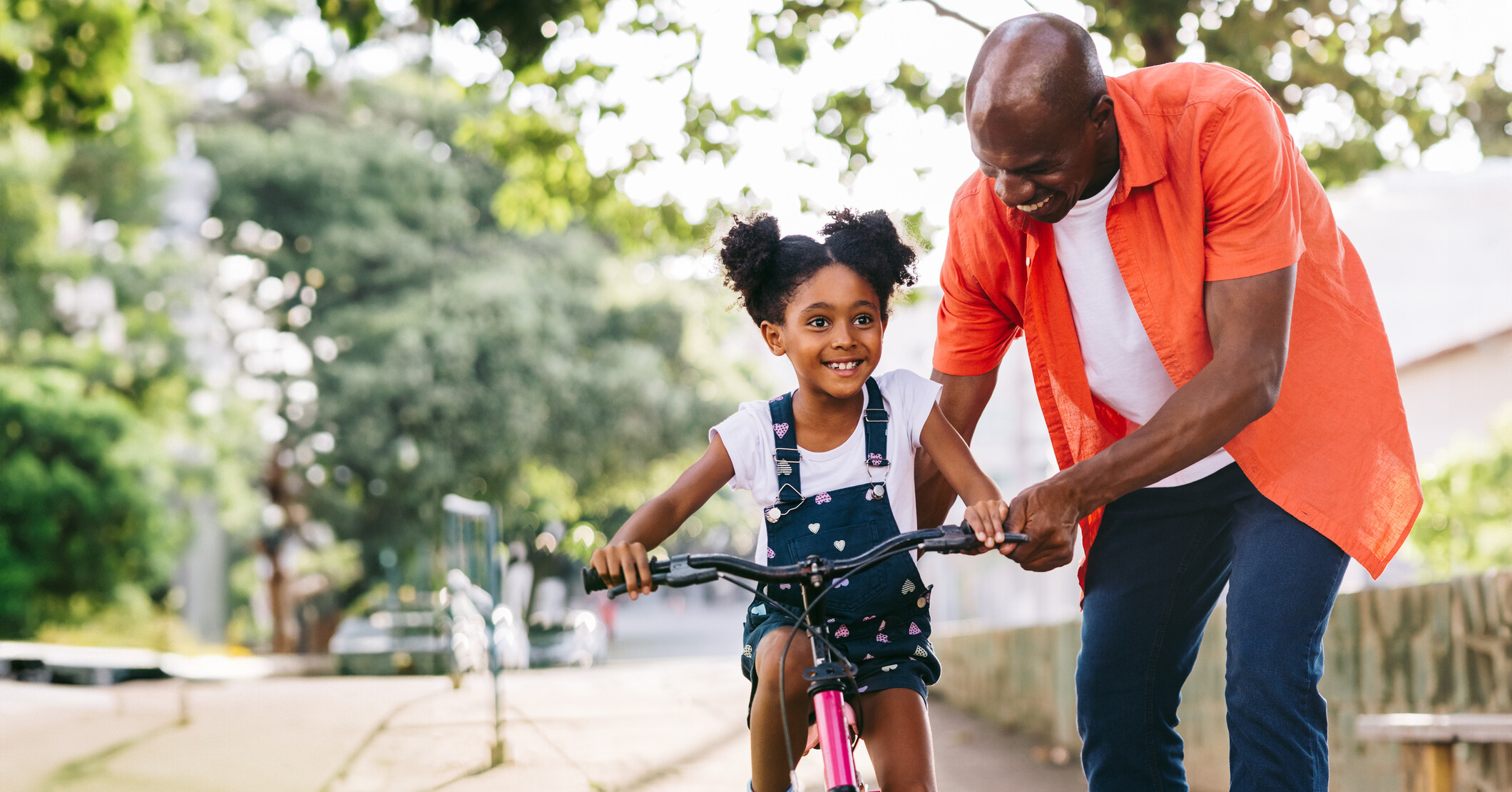 Father teaching daughter how to ride a bicycle in a park.