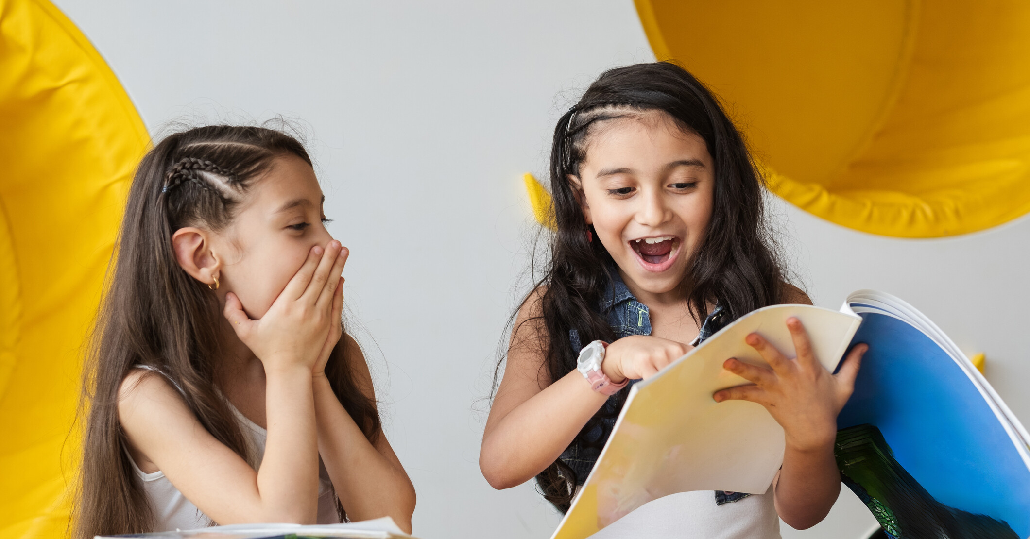 Two elementary age girls reading a funny book.