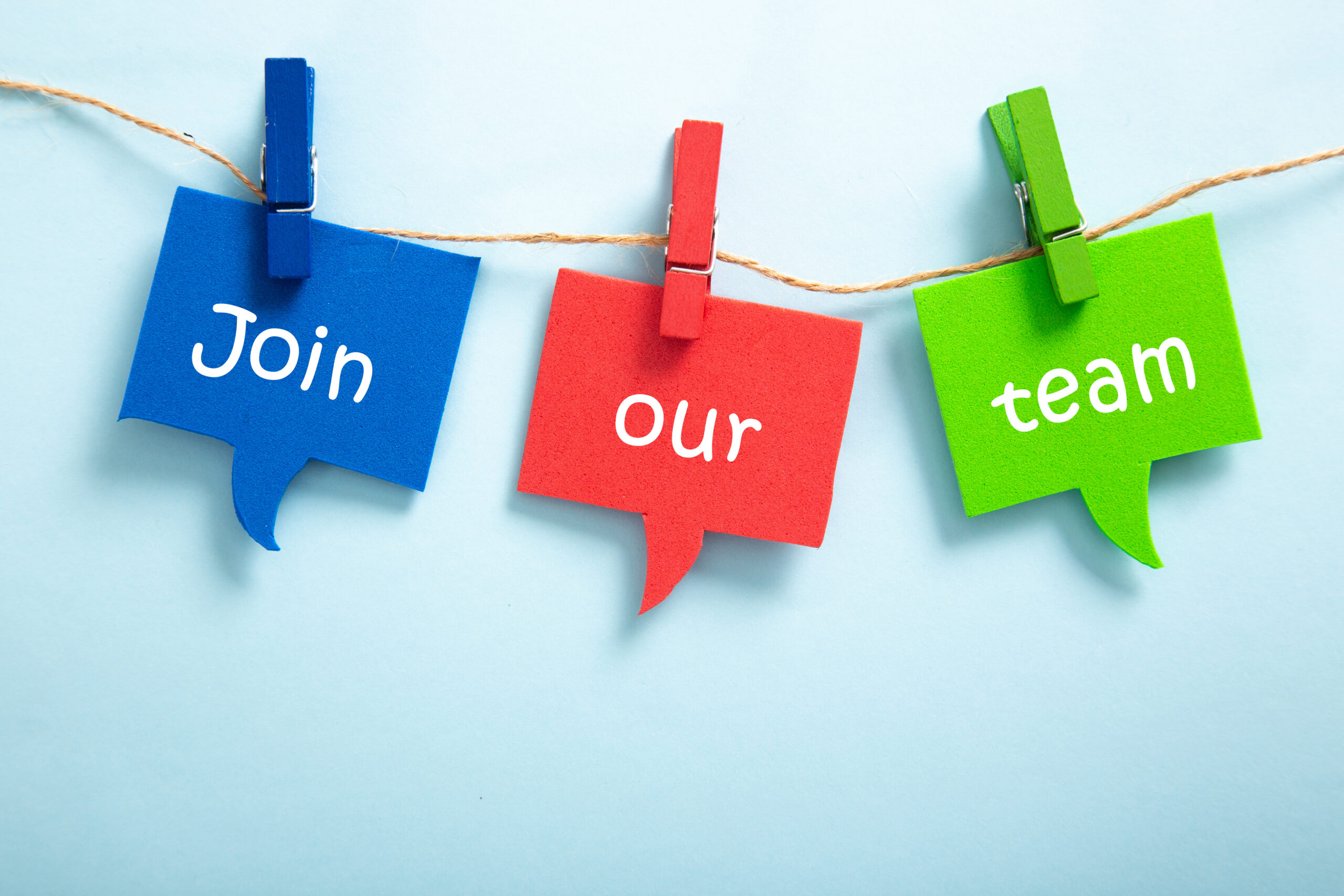 the text says join our team which is represented by blue, red, and green post it notes hanging on a clothes line