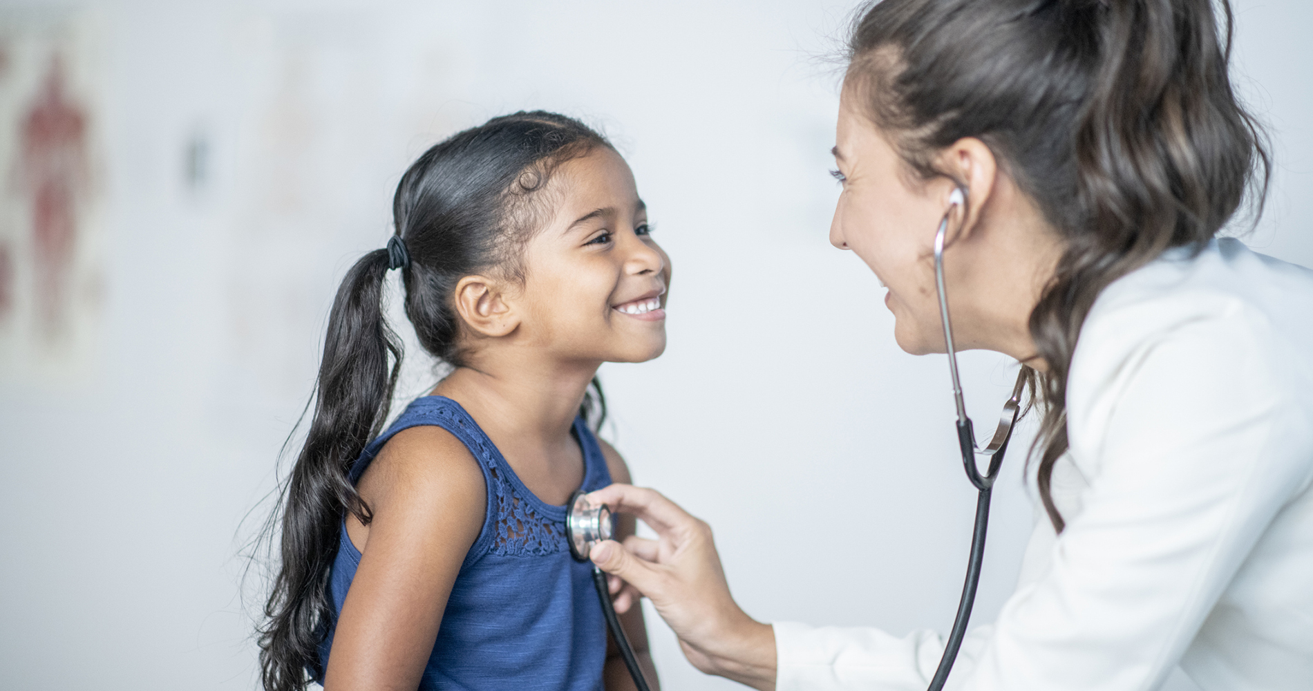 Elementary-aged girl with a stethoscope check from a female medical provider. Exterior view of Ronald McDonald Care Mobile.