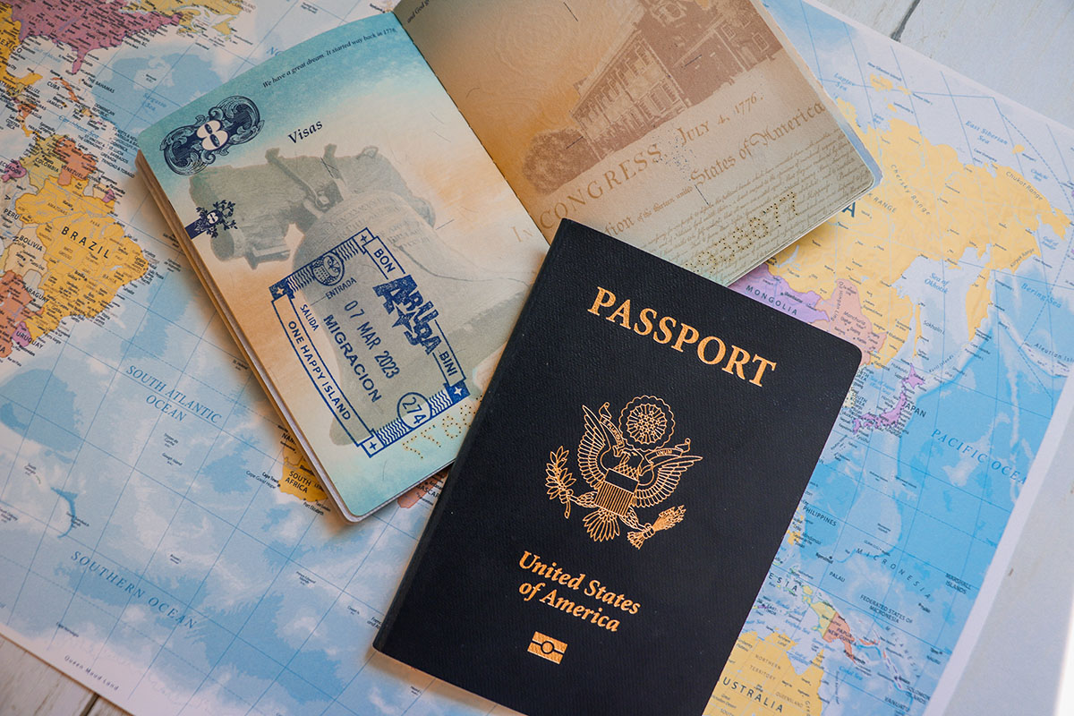 passports-1 Two passports lay on top of a world map. The first passport is open and shows a stamp from traveling. The other passport is closed and says "Passport, United States of America."